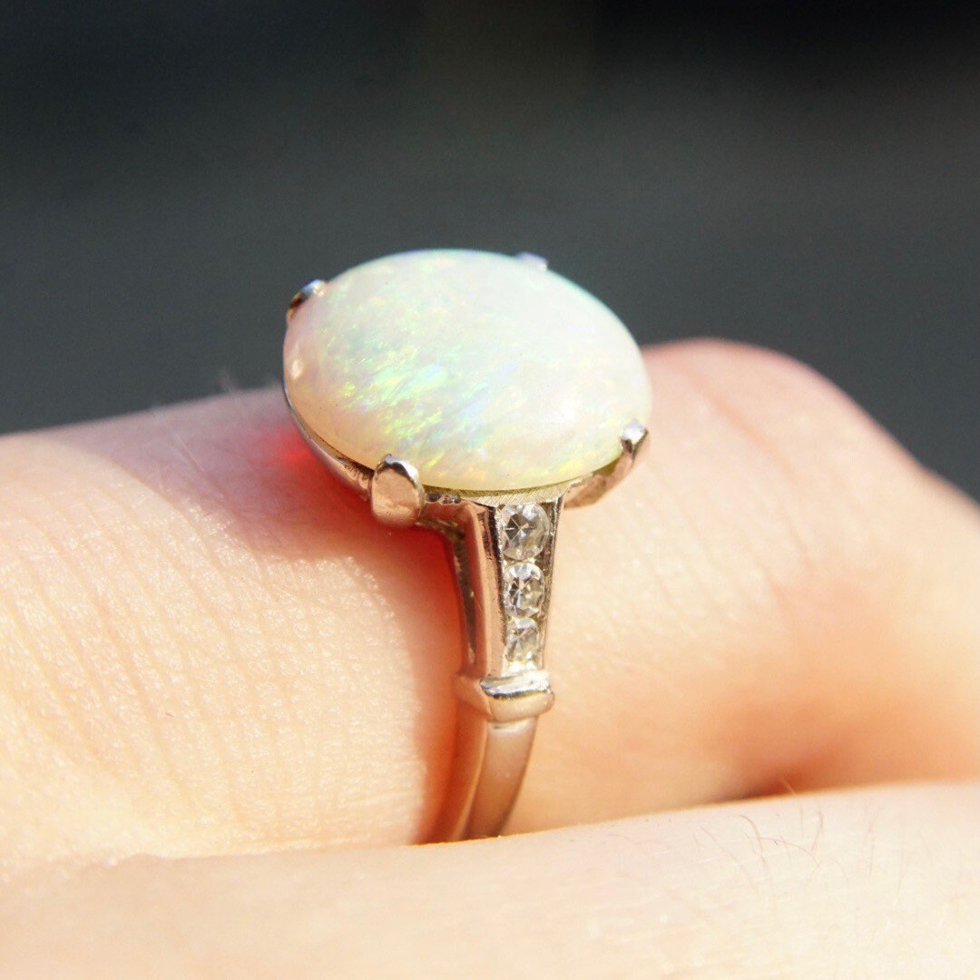 Vintage 14K white gold ring with an iridescent white opal stone and accent diamonds in a cathedral setting, shown on a finger.