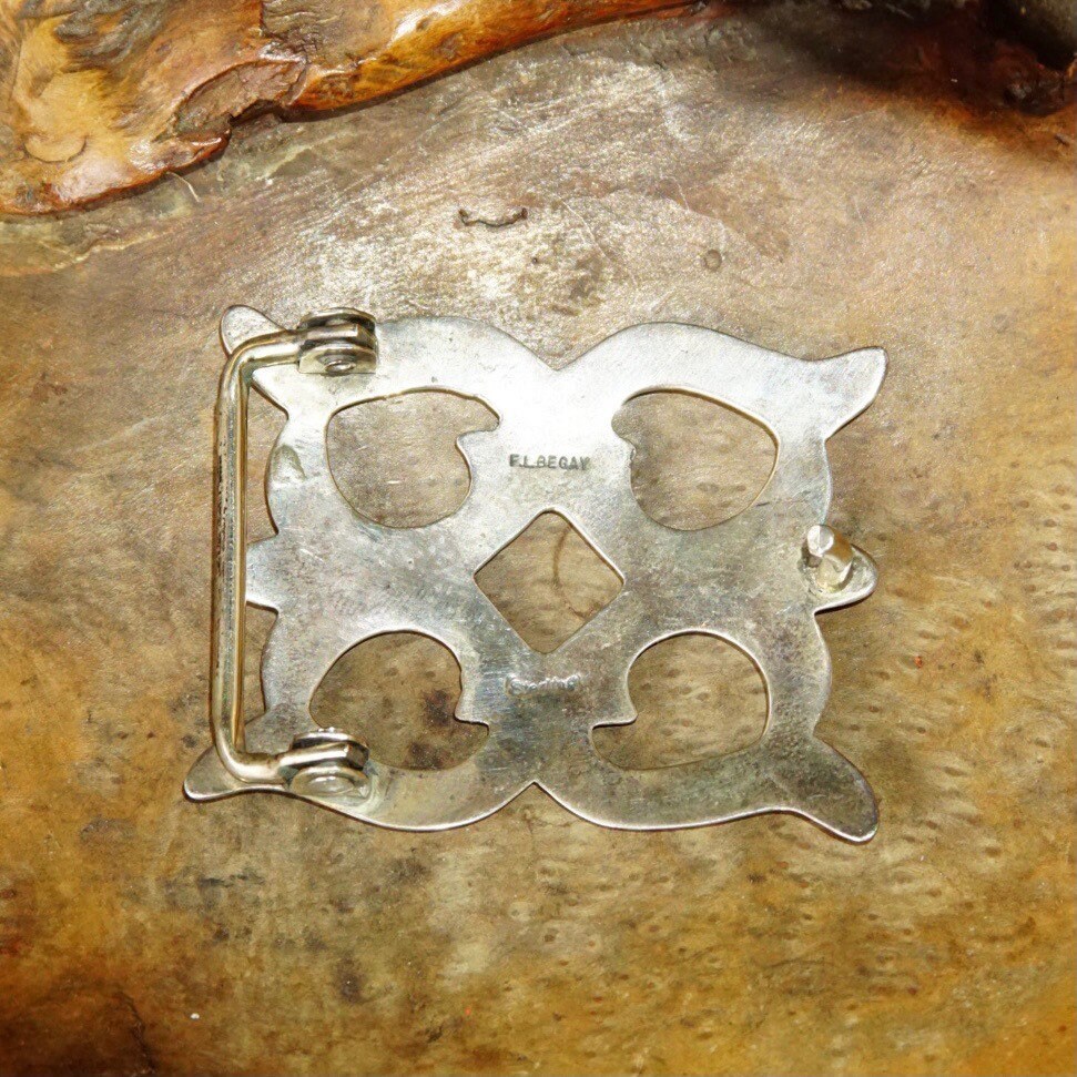 Vintage Navajo sand cast sterling silver belt buckle with abstract cutout design and maker's hallmark, displayed on weathered metal surface