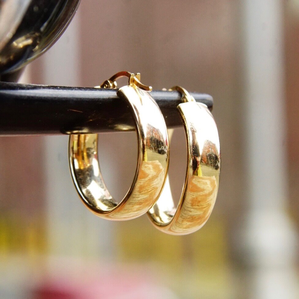 Vintage 14K yellow gold latch back hoop earrings from Saks Fifth Avenue, measuring 1 1/2 inches long, hanging on a black metal stand.