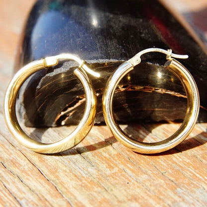 Vintage 14K yellow gold hoop earrings with latch back closure, signed Sakes Fifth Avenue, resting on wooden surface.