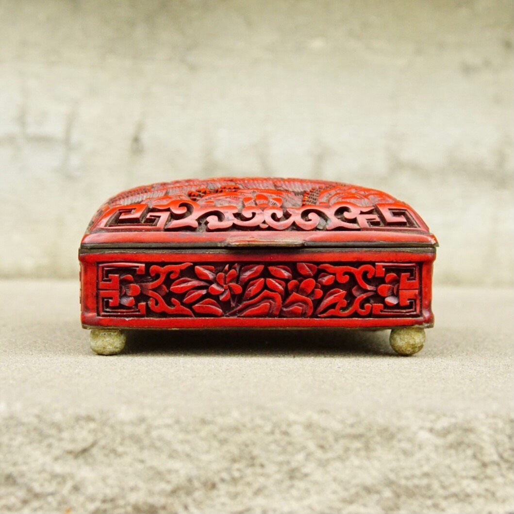 Antique Chinese carved cinnabar lacquer box with intricate floral and landscape designs on lid and sides, featuring brass feet and hinged opening, measuring 4 inches wide, 3.5 inches deep and 2 inches high.