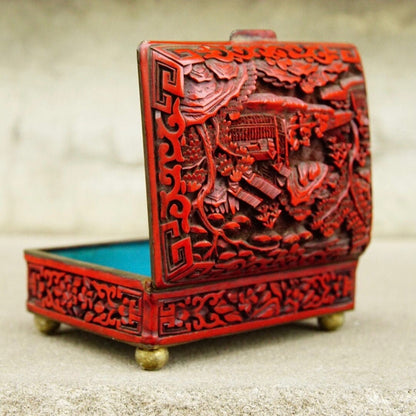 Intricately carved antique Chinese cinnabar lacquer box with hinged lid depicting detailed figural landscape and flora/fauna motifs in vibrant red, measuring 4 inches wide, 3.5 inches deep and 2 inches high.