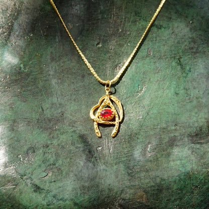 Vintage 14K gold wishbone heart pendant necklace with faceted ruby on a thin gold chain, against a weathered green background.