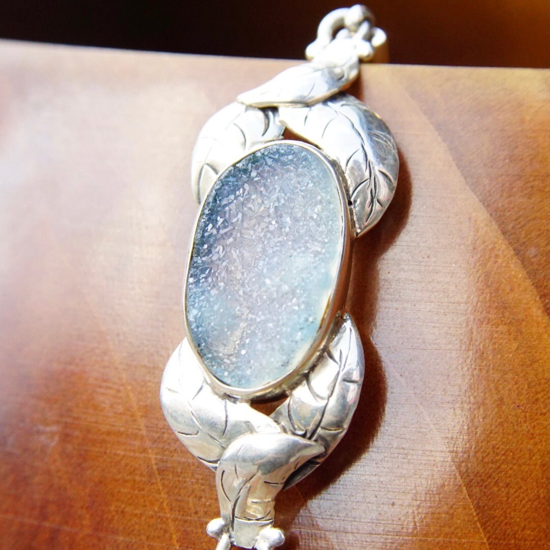 Vintage sterling silver bracelet featuring an oval blue druzy quartz gemstone encased in textured silver leaves, with an adjustable rope chain design.