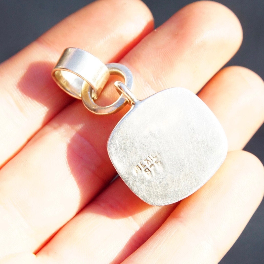 Silver and malachite pendant held in hand, showing textured oval silver pendant with inset banded malachite stone, double loop bail for necklace attachment. Vintage Mexican Taxco 925 sterling silver modernist design.