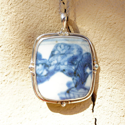 Vintage sterling silver pendant featuring an inlaid blue and white ceramic pottery shard, framed in an ornate silver setting, measuring approximately 2 3/4 inches in length.