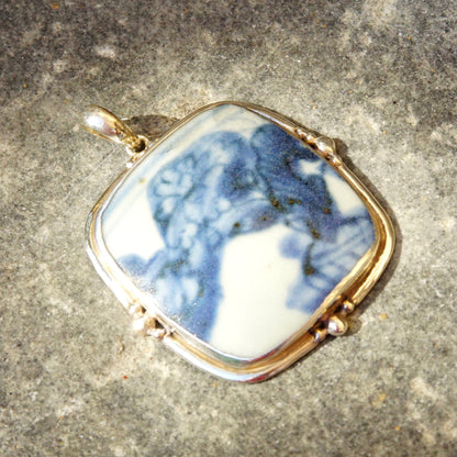 Vintage sterling silver pendant with inlaid blue and white ceramic pottery shard, large 2 3/4 inch pendant set in ornate silver frame against textured gray background.