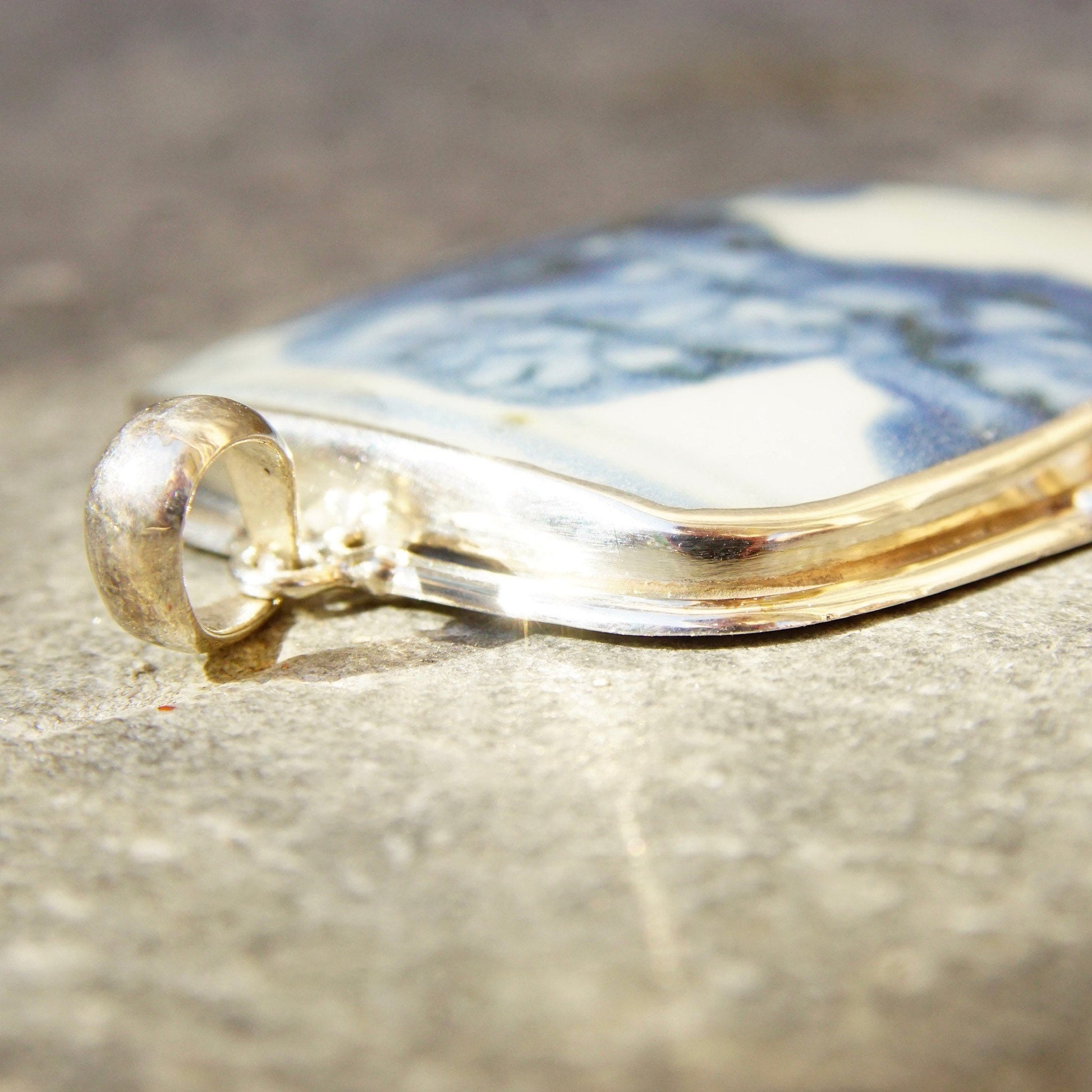 Vintage sterling silver pendant with inlaid blue and white ceramic pottery shard, measuring 2 3/4 inches long, featuring a large porcelain fragment framed in silver.