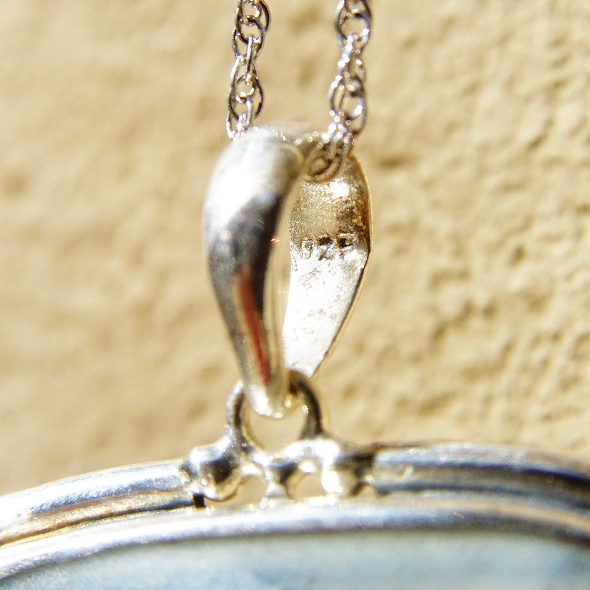 Vintage sterling silver pendant with inlaid blue and white ceramic pottery shard, large 2 3/4 inch long pendant with antique porcelain piece set in silver frame, dangling from silver chain against textured beige background.