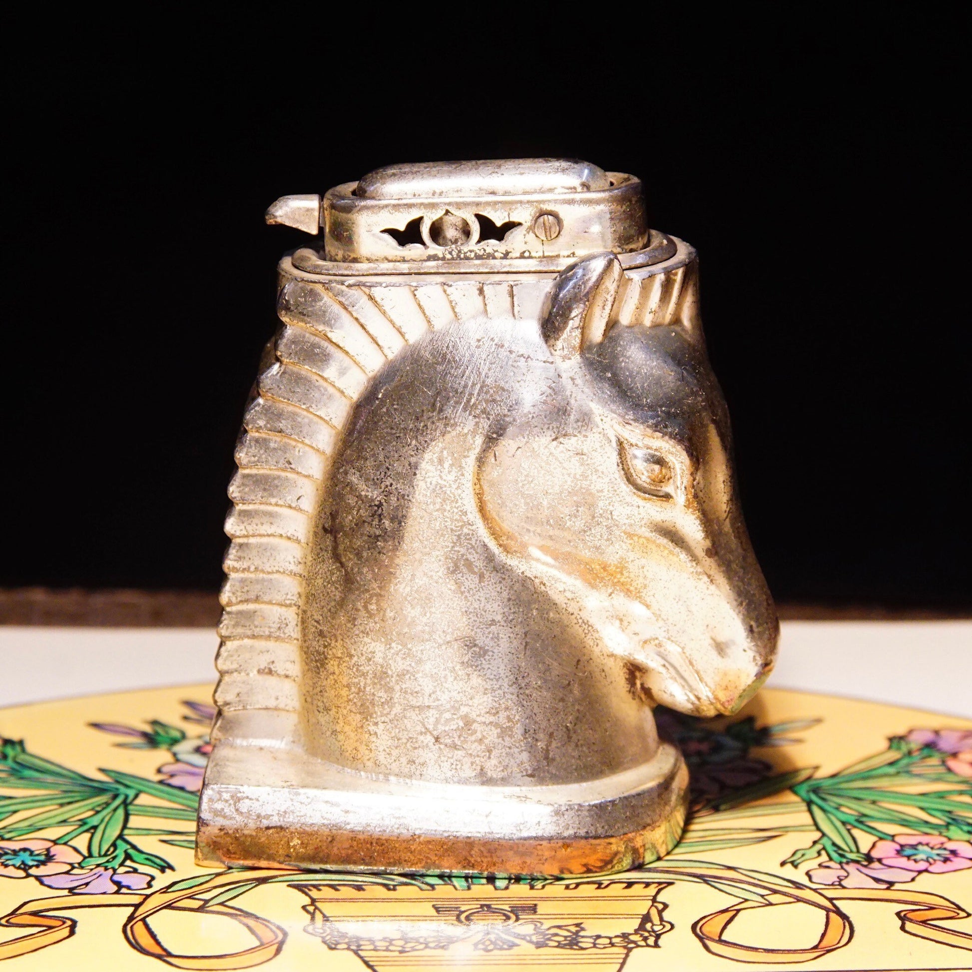 Vintage silver-plated horse head table lighter made in Occupied Japan, collectible butane lighter measuring 2 3/4 inches, not tested for functionality, displayed on floral design surface.