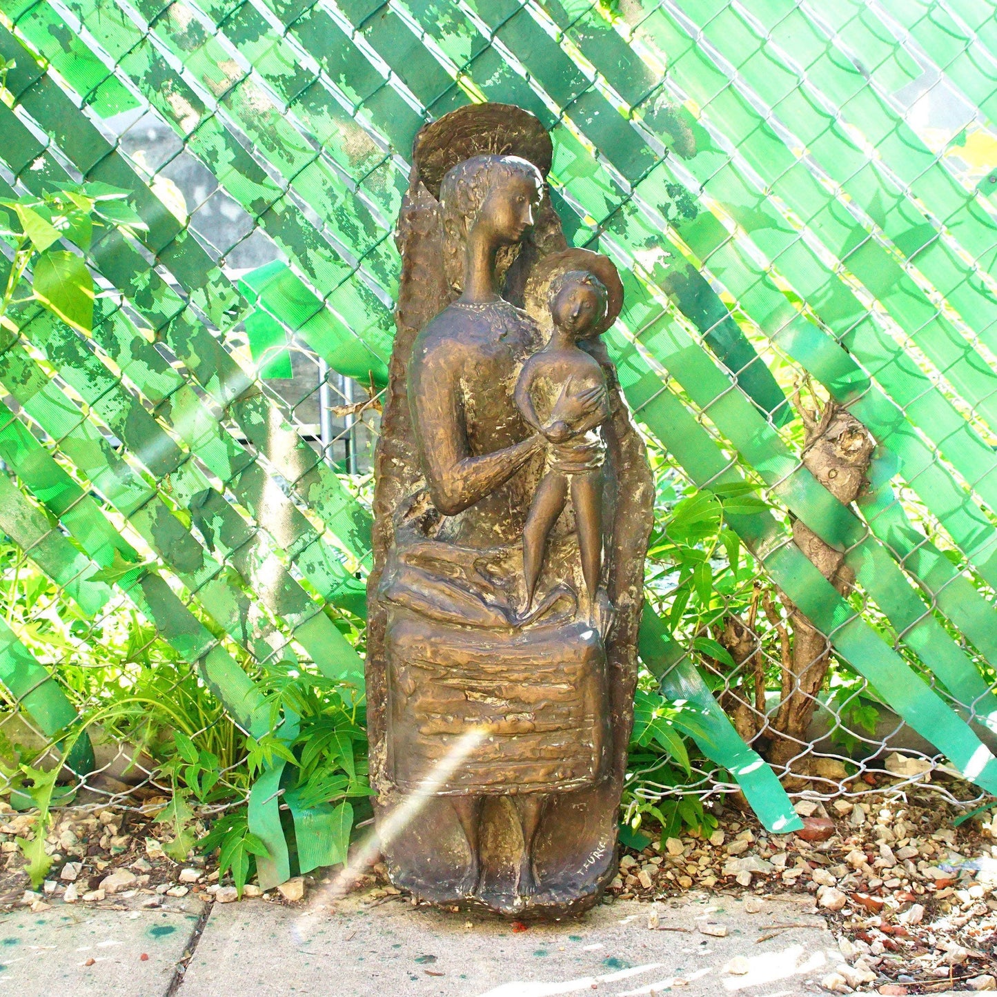 Vintage bronze sculpture depicting an abstract, stylized Mother Mary holding baby Jesus, created by Italian artist Toni Furlan. The statue has an aged patina and stands approximately 36 inches tall, set against a vibrant green tiled background.