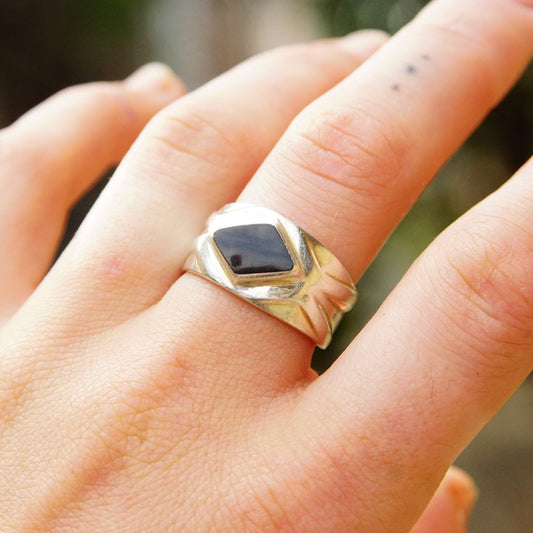 Vintage sterling silver ring with black stone on hand, displaying textured silver band and diamond-shaped stone setting.