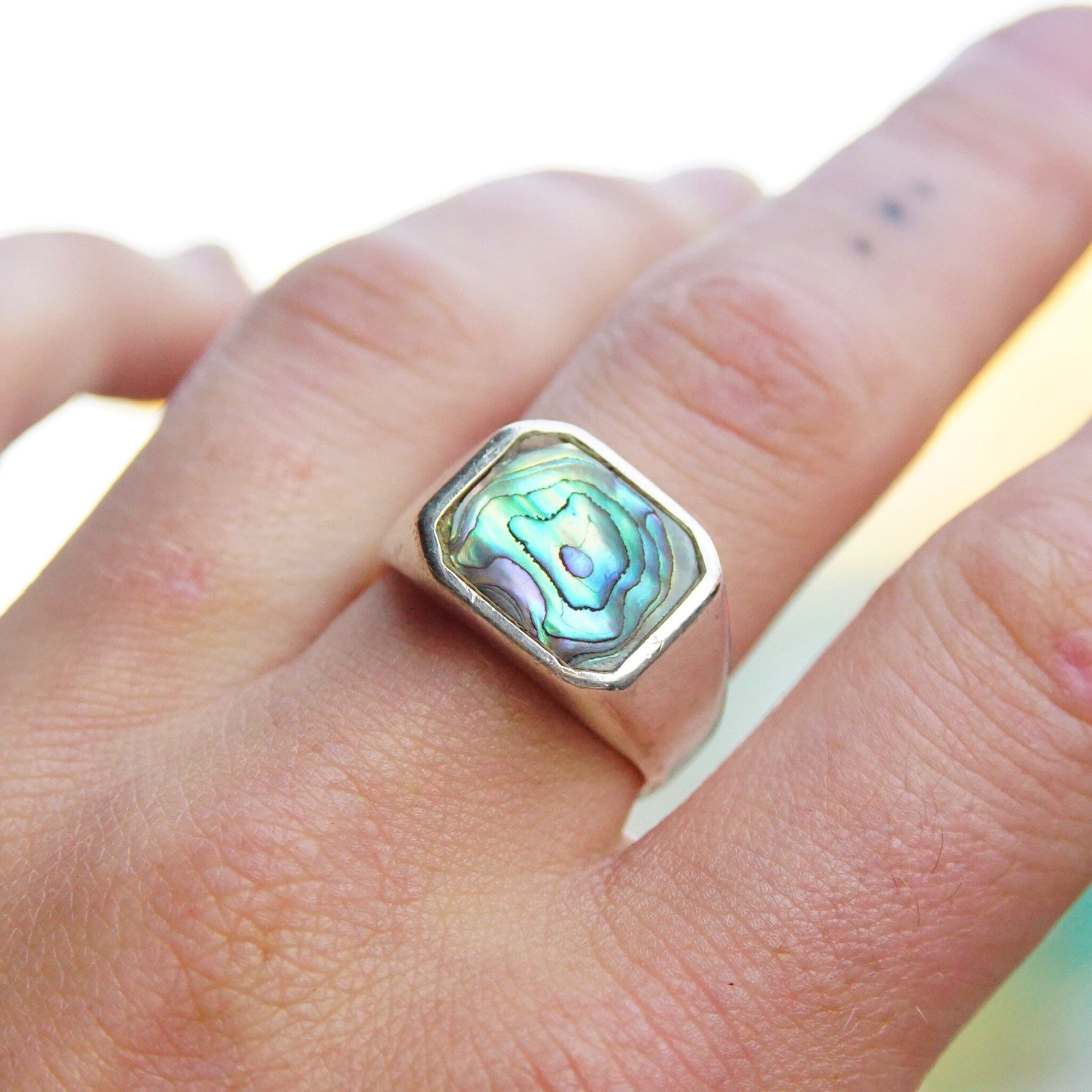 Vintage sterling silver abalone inlay signet ring with iridescent snail shell design on a hand, unisex jewelry in size 9 1/2 US.