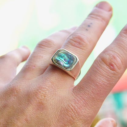 Vintage sterling silver signet ring with iridescent abalone shell inlay, shown on a hand against a light green background. Unisex ring jewelry in a men's size 9 1/2 US.