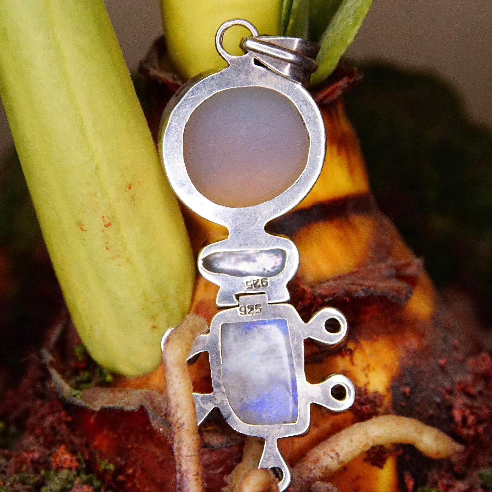 Vintage abstract modernist sterling silver pendant featuring moonstone, mother of pearl, quartz and purple/blue gemstones in a hinged design, measuring 3 1/8 inches long, shown with a green banana for scale.