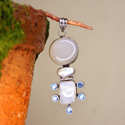 Vintage abstract modernist sterling silver pendant featuring moonstone, mother of pearl, quartz, and purple/blue gemstones, measuring 3 1/8 inches long, shown hanging from a branch against a neutral background.