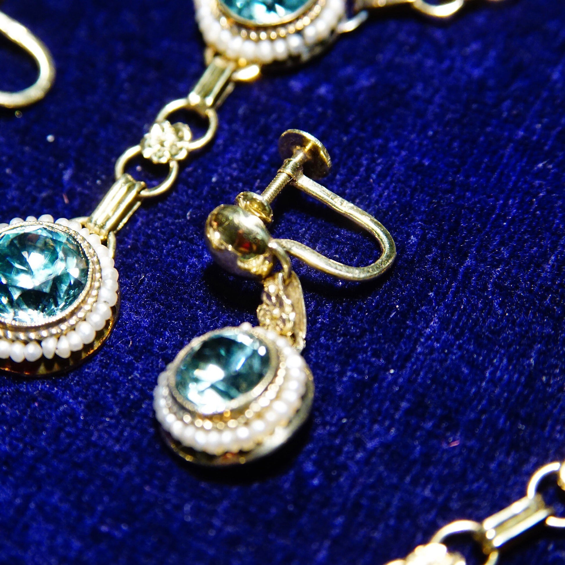 Vintage 14K gold aquamarine and seed pearl jewelry set featuring brilliant blue gemstones, including a matching Y-pendant necklace, bracelet, screw back earrings, and brooch, displayed on a dark blue textured background.