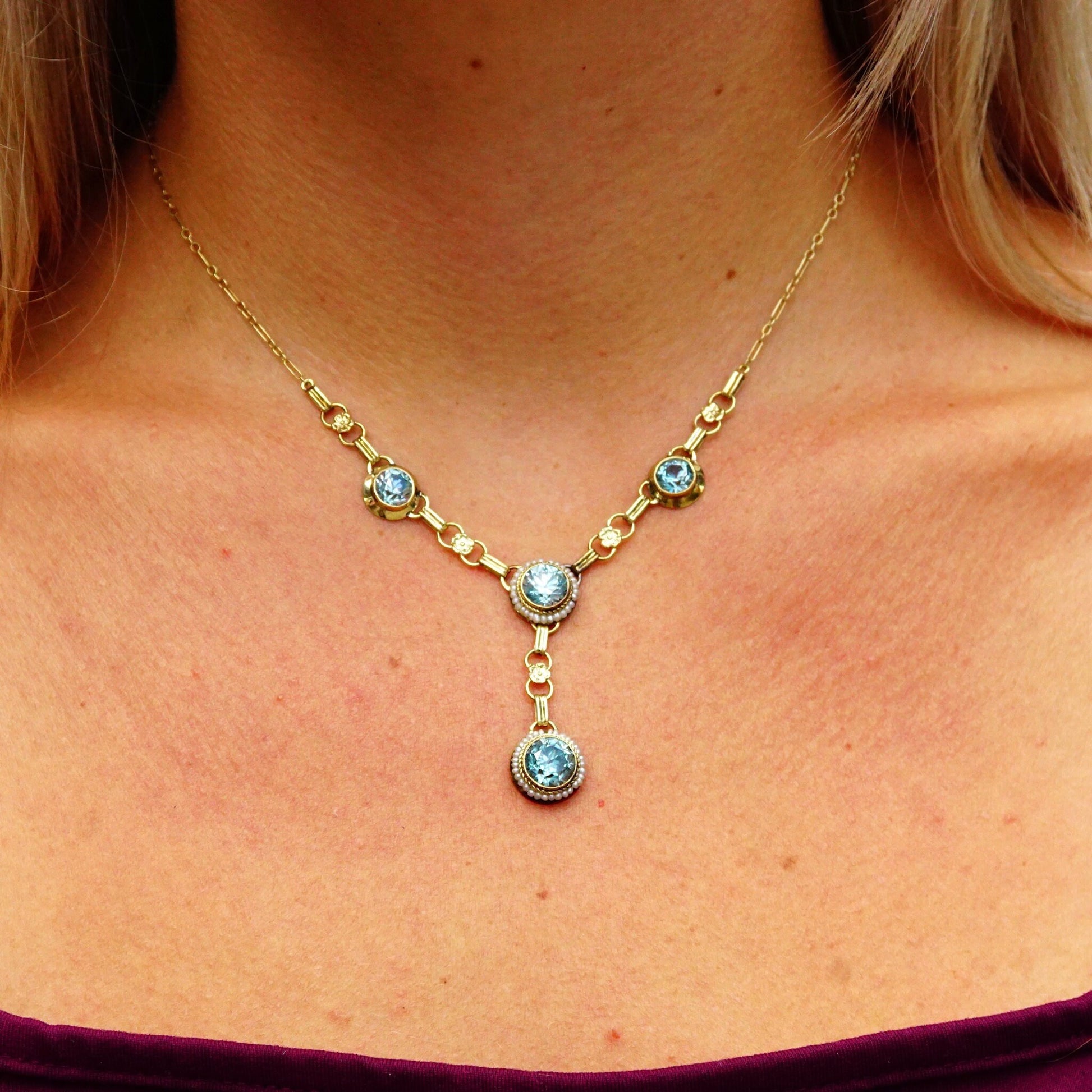 Vintage 14K gold aquamarine and seed pearl jewelry set worn on a woman's neck, featuring a Y-pendant necklace, bracelet, screw back earrings and brooch with brilliant blue gemstones.