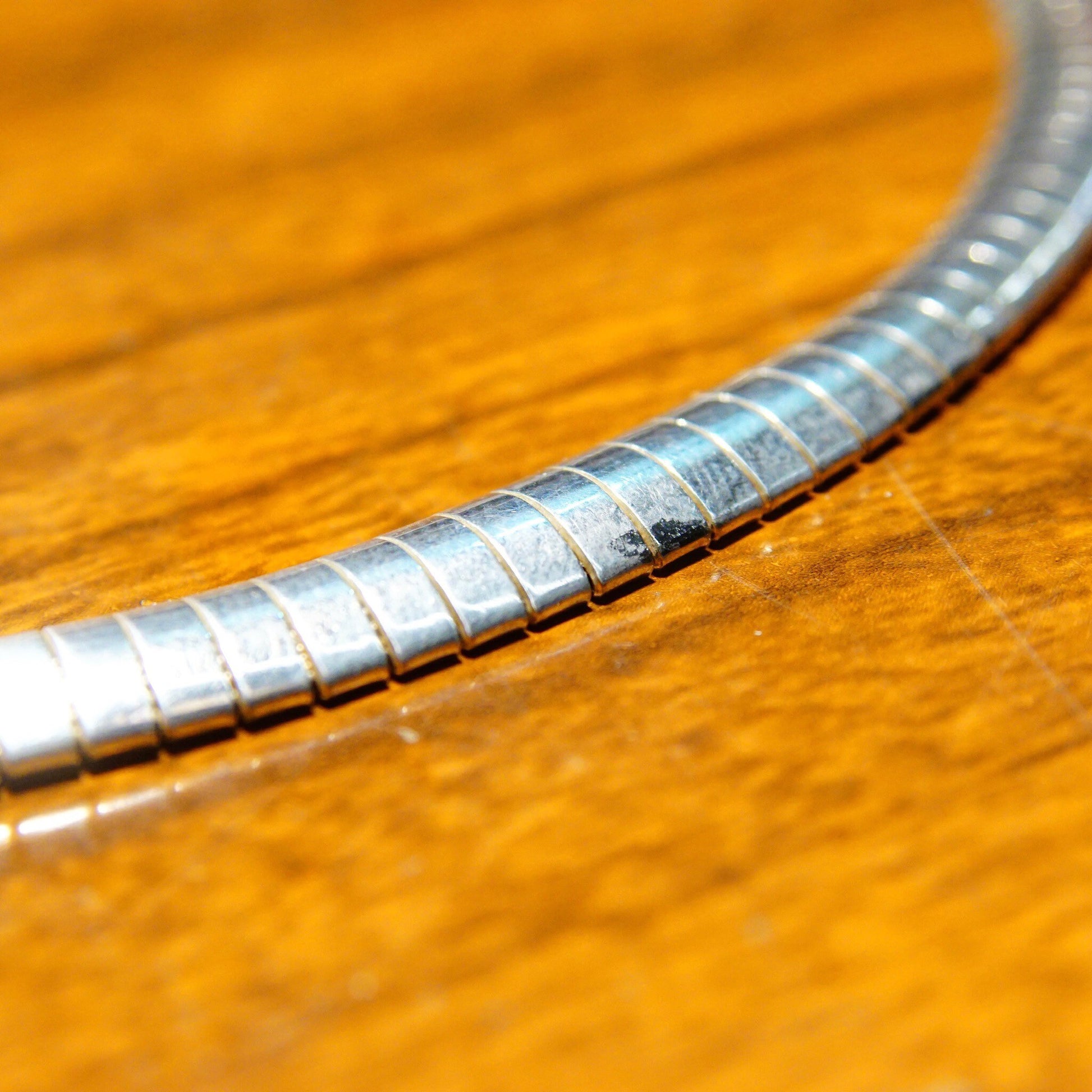 Vintage sterling silver omega collar necklace with modernist design, 7.25 mm omega link chain, lobster claw clasp, made in Italy 925, measuring 16 1/4 inches long, photographed on wooden surface.