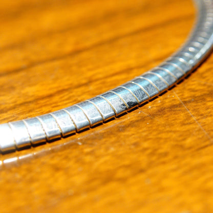 Vintage sterling silver omega collar necklace with modernist design, 7.25 mm omega link chain, lobster claw clasp, made in Italy 925, measuring 16 1/4 inches long, photographed on wooden surface.