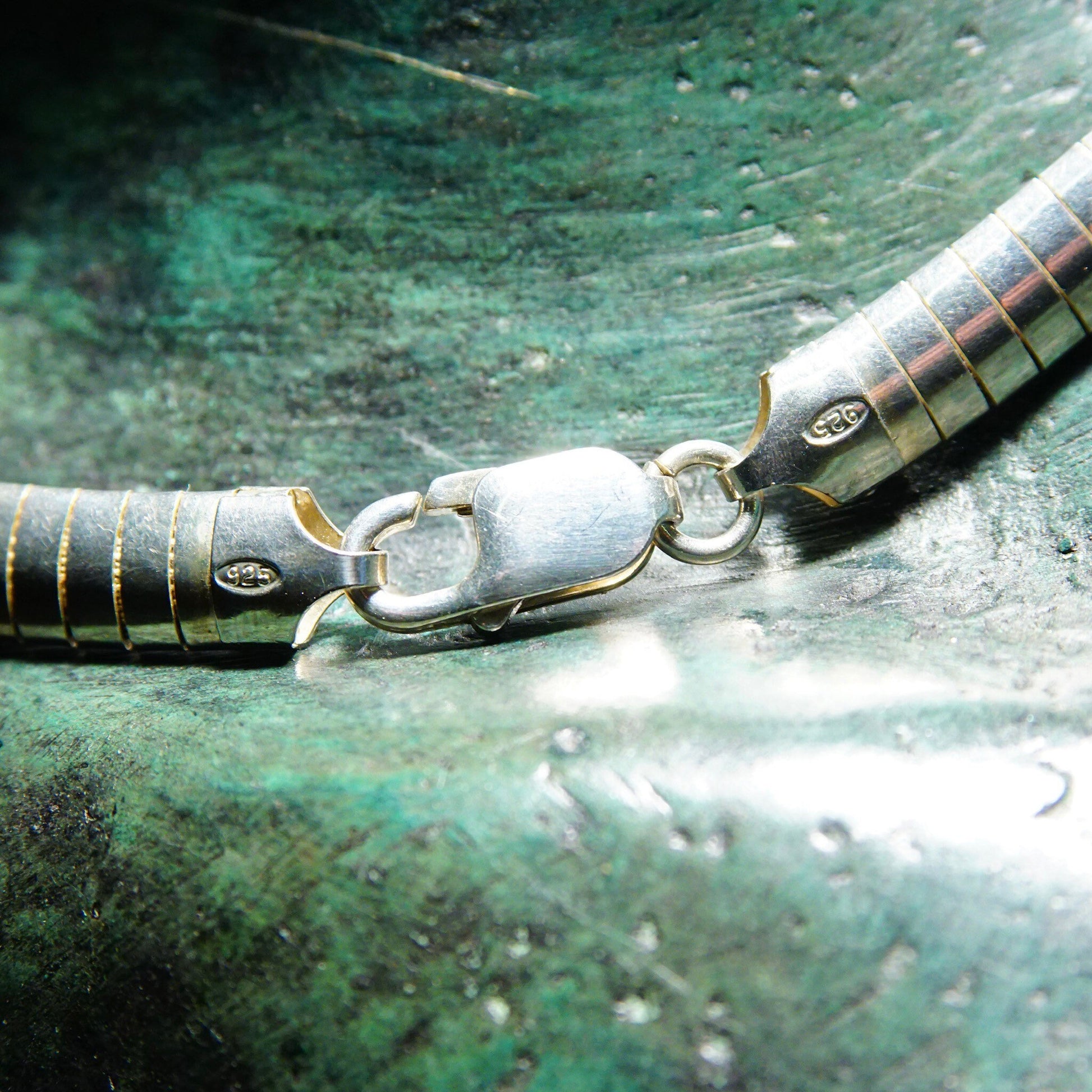 Vintage sterling silver omega collar necklace with lobster claw clasp, on textured green metallic surface.