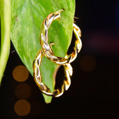 Vintage 14K yellow gold twisted hoop earrings featuring a puffed repousse wreath design against a black background with blurred green leaf in the foreground.