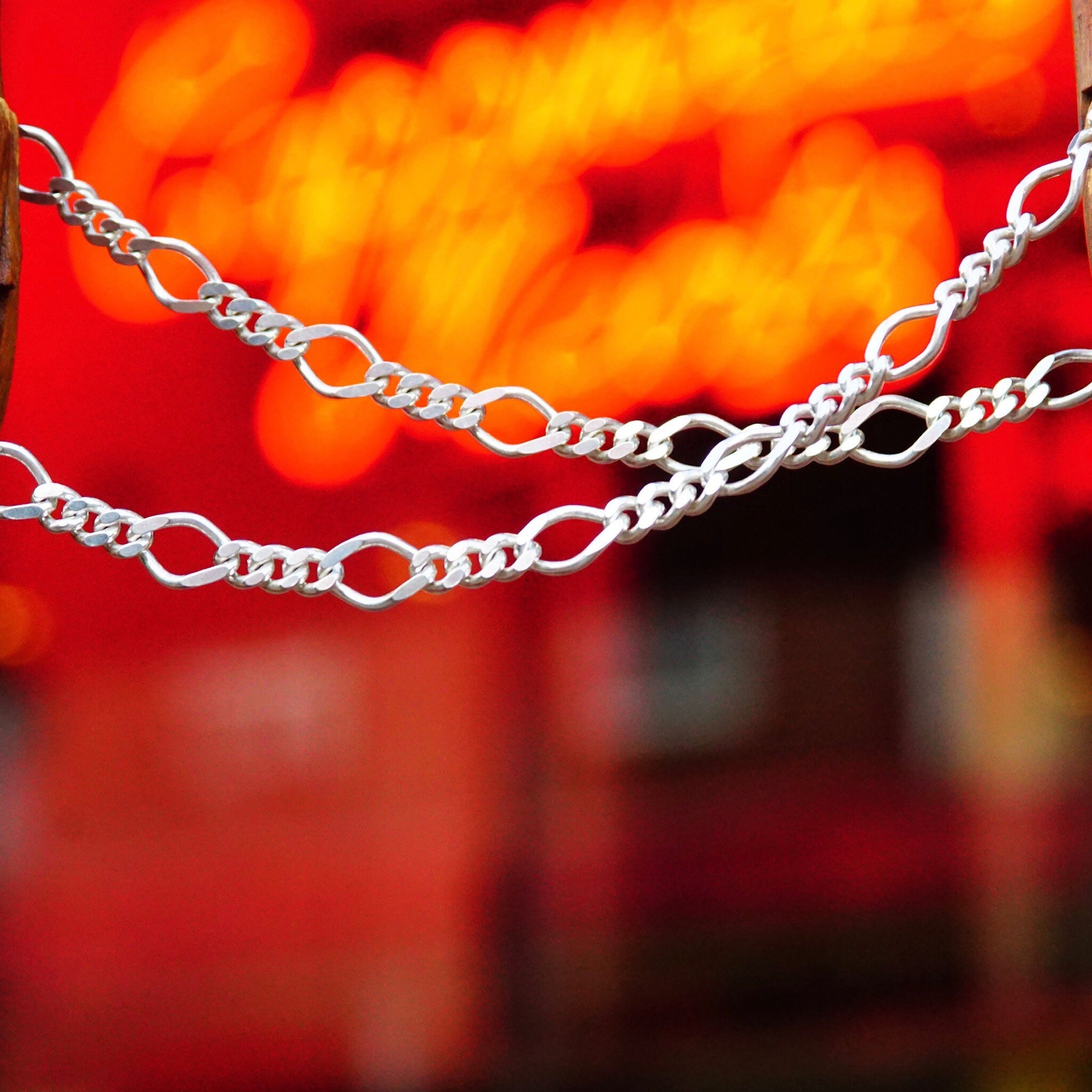 Shiny sterling silver figaro chain necklace with alternating curb and long links against a bright red and orange blurred background