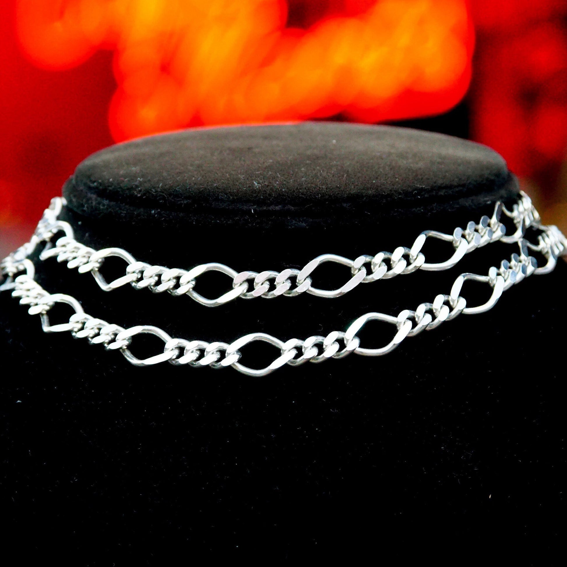 Vintage Milor 925 sterling silver figaro chain necklace with alternating 5mm curb links and 8.5mm long links against a black jewelry display and blurred red background.