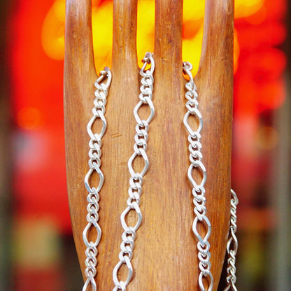 Silver figaro chain necklace with alternating curb and long links hanging in front of blurred red and orange background