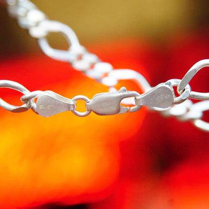 Macro close-up of shiny sterling silver figaro chain necklace with alternating curb and long links on blurred red background