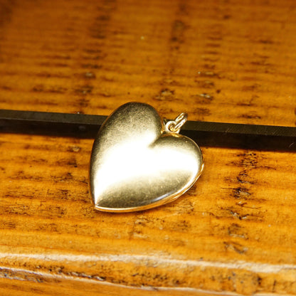 14K gold antique heart locket pendant necklace with a small diamond, open on a wooden surface to show two empty photo frames inside.