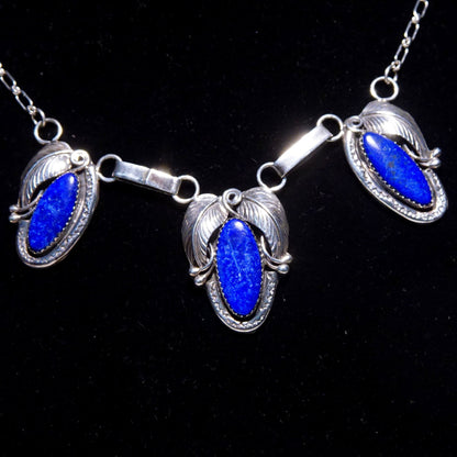 Vintage Native American sterling silver lapis lazuli pendant necklace featuring a three-stone pendant with engraved leaf settings, suspended from an oval link chain measuring 20 3/4 inches in length, showcasing deep blue oval lapis lazuli gemstones set in ornate sterling silver.