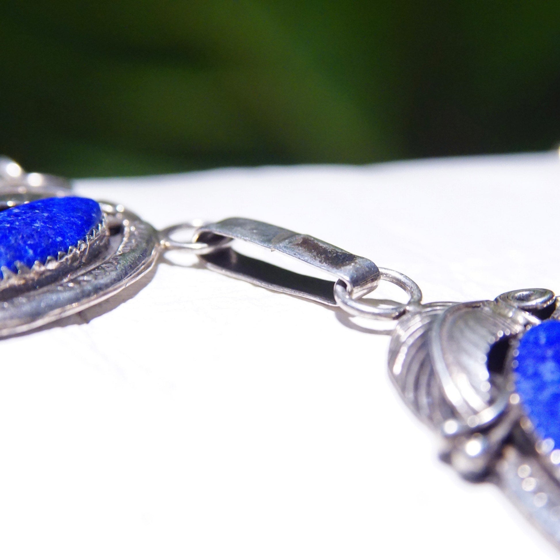 Vintage Native American sterling silver necklace with three lapis lazuli stones in engraved leaf settings on an oval link chain against a white background.