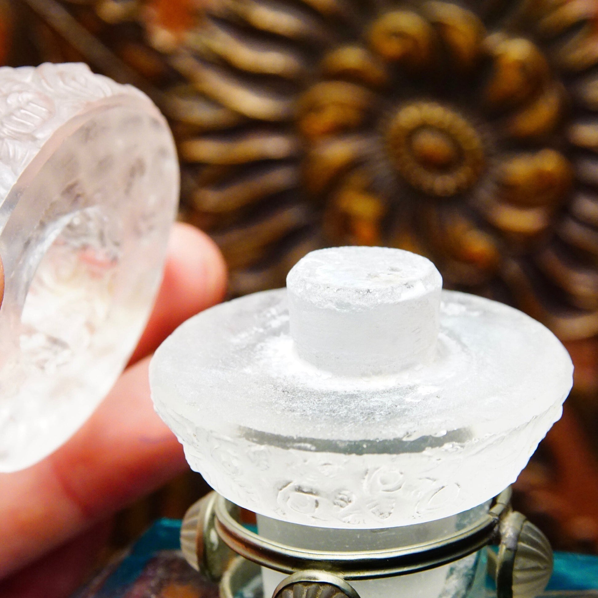 Antique 1920's Austrian crystal perfume bottle with frosted glass figural dauber and carved glass stopper, featuring pewter mounts, measuring 8 inches tall, displayed with pine cone decorations in background.