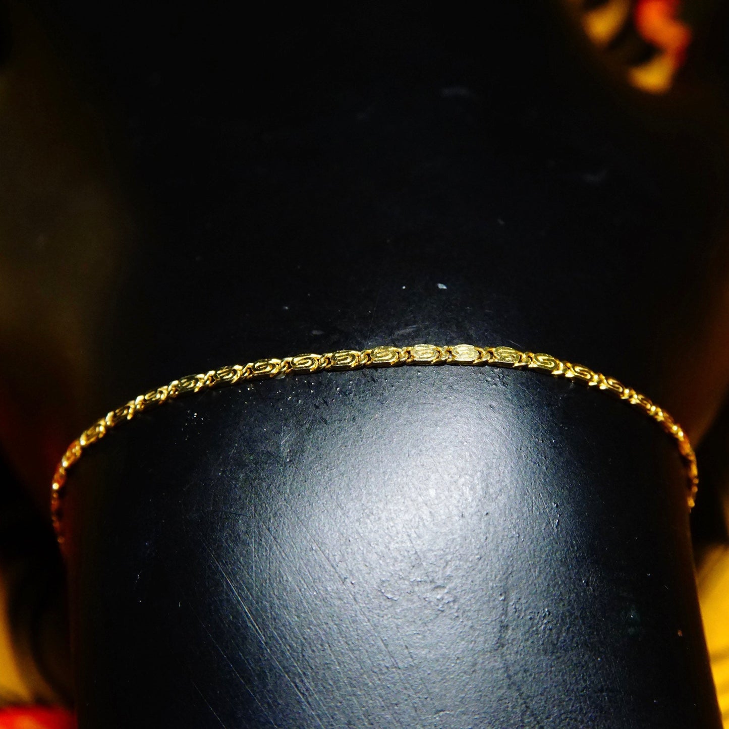 Vintage 14k yellow gold snail chain bracelet with delicate 1.5mm swirl links, displayed on a black surface with warm lighting creating a soft glow on the gold.