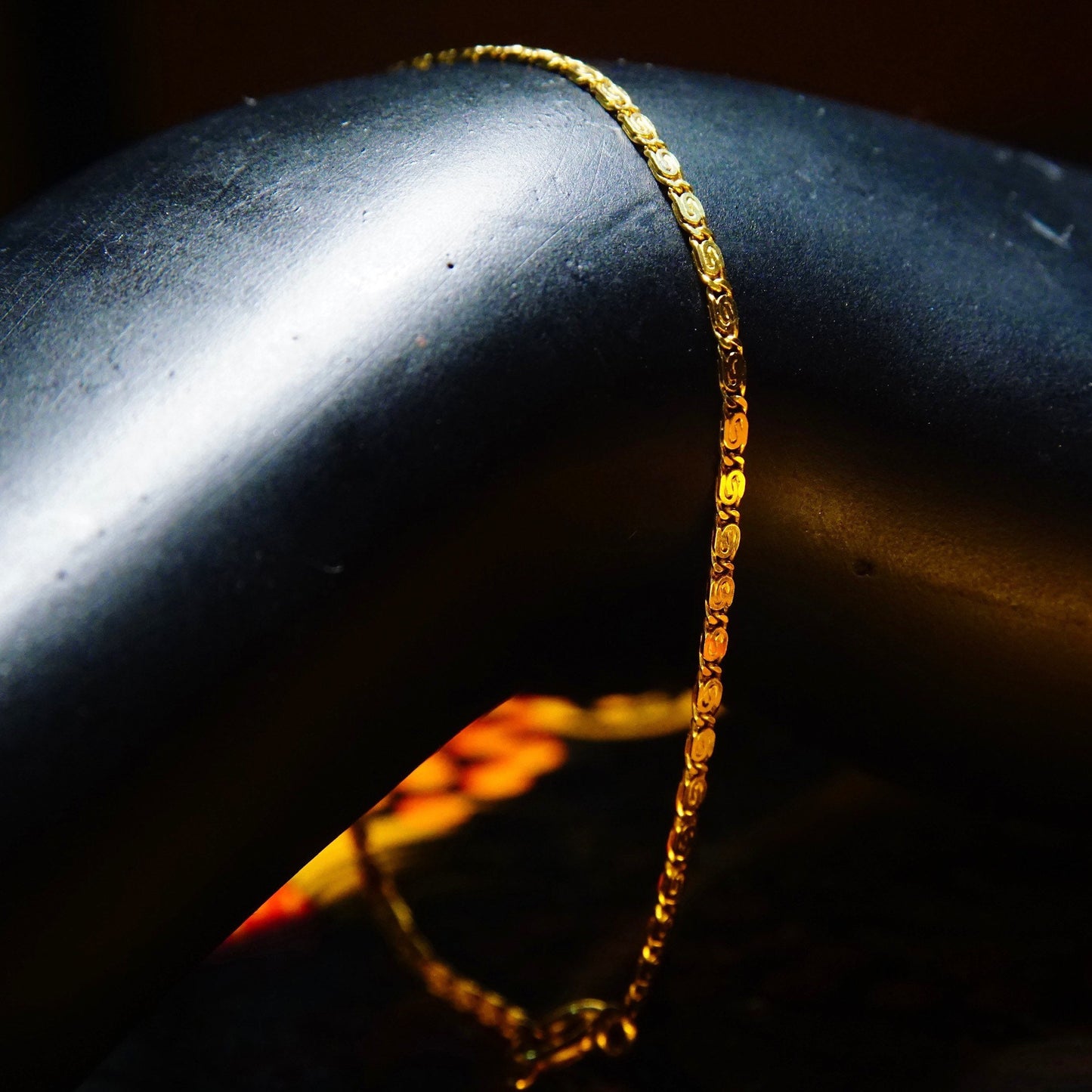 Delicate vintage 14k yellow gold snail chain bracelet with swirl links, photographed with dramatic lighting on a black reflective surface.