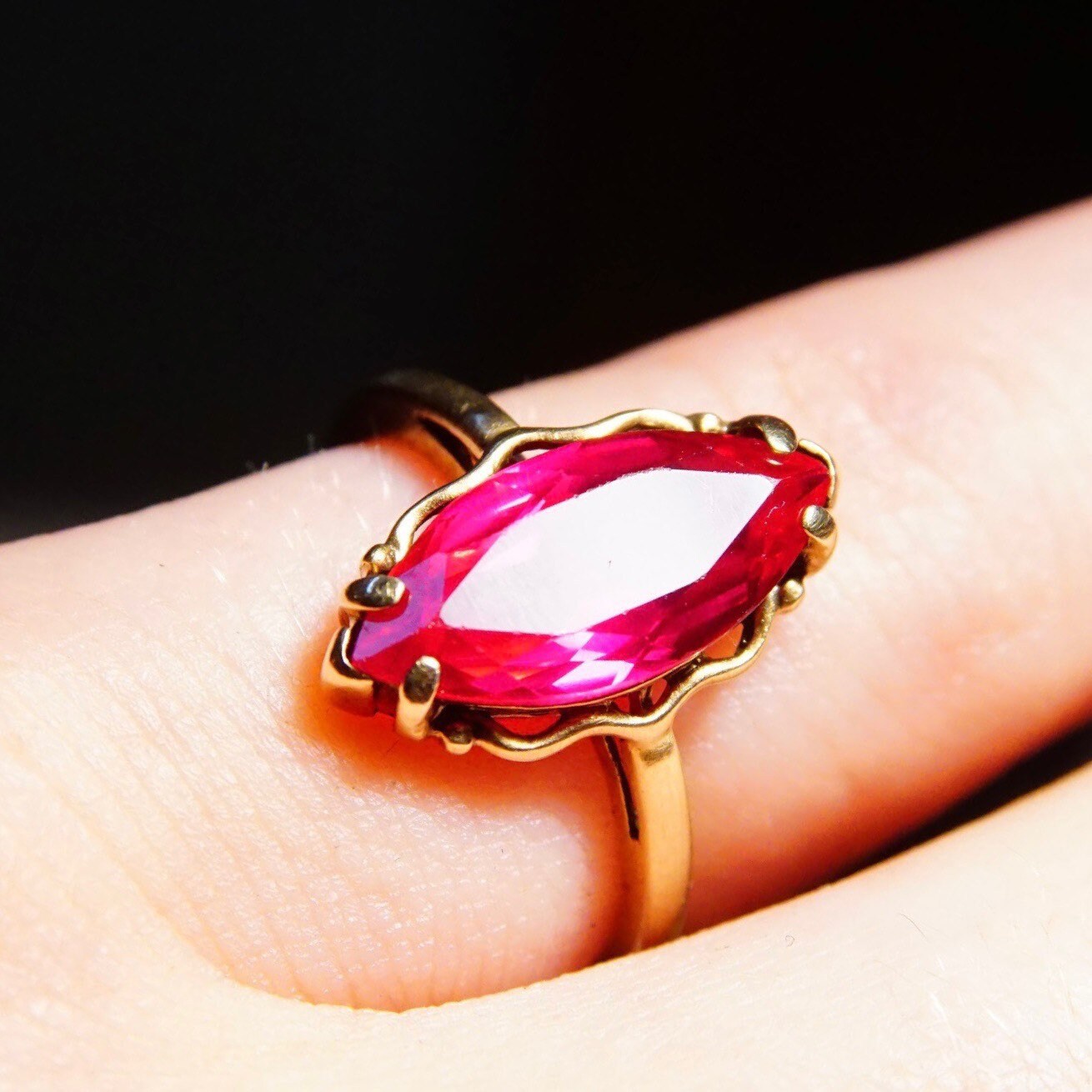 Antique 10K yellow gold ring featuring a faceted marquise-cut ruby gemstone set in an elegant straight band design, shown on a finger against a black background, ring size 6 1/4 US.