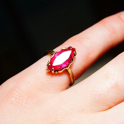 Antique 10K yellow gold marquise-cut ruby ring with faceted red gemstone on a straight gold band, ring size 6 1/4 US, shown on a finger against a black background.