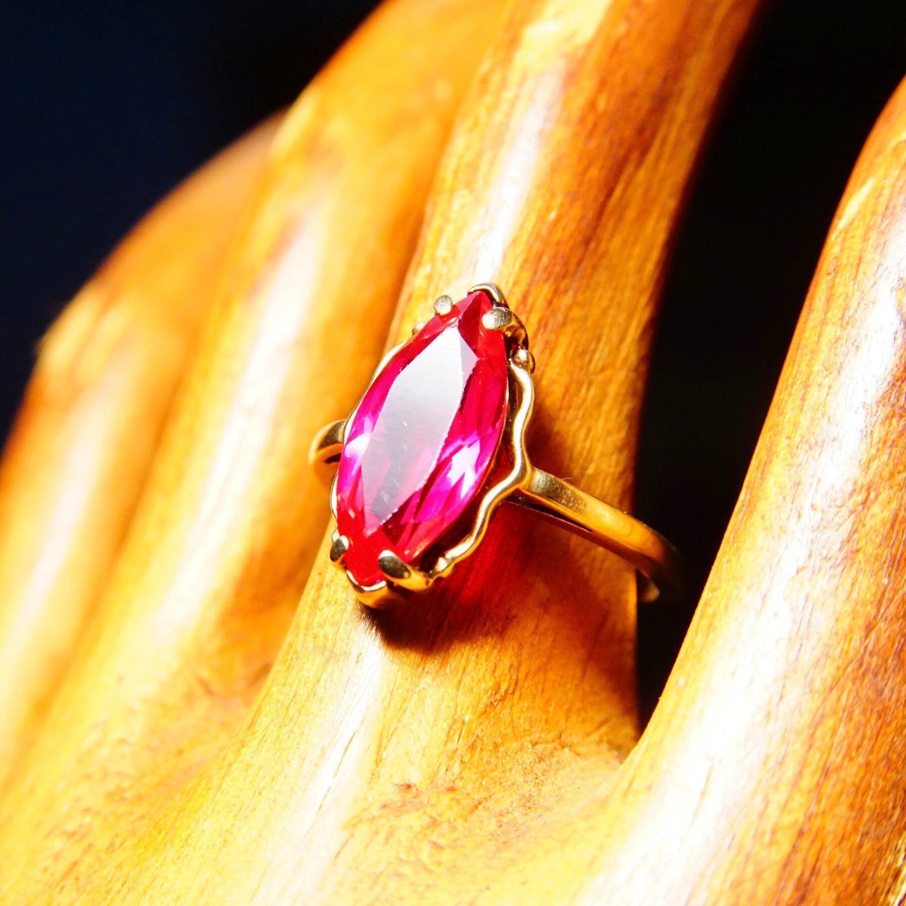 Antique 10K yellow gold marquise ruby ring featuring a faceted red gemstone set on a straight gold band, size 6 1/4 US, displayed on wooden surface.