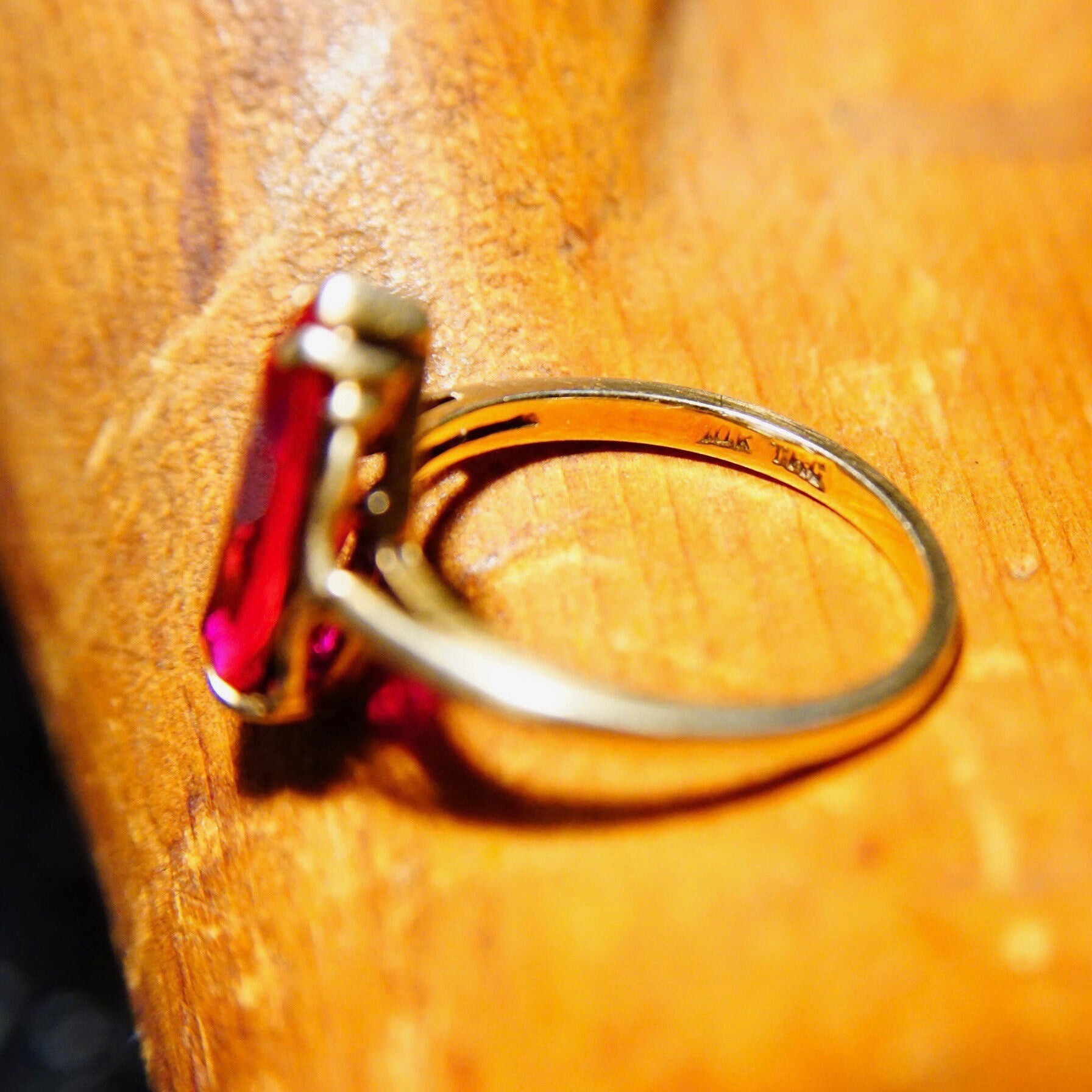 Antique 10K yellow gold marquise ruby ring with faceted red gemstone on a straight gold band, showcasing intricate details on worn wooden surface, size 6 1/4 US.