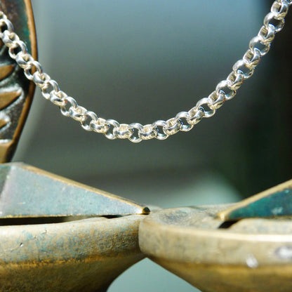 Vintage sterling silver rolo chain necklace with interlocking bead links, close-up view showing heavy silver chain details against blurred blue-green background.