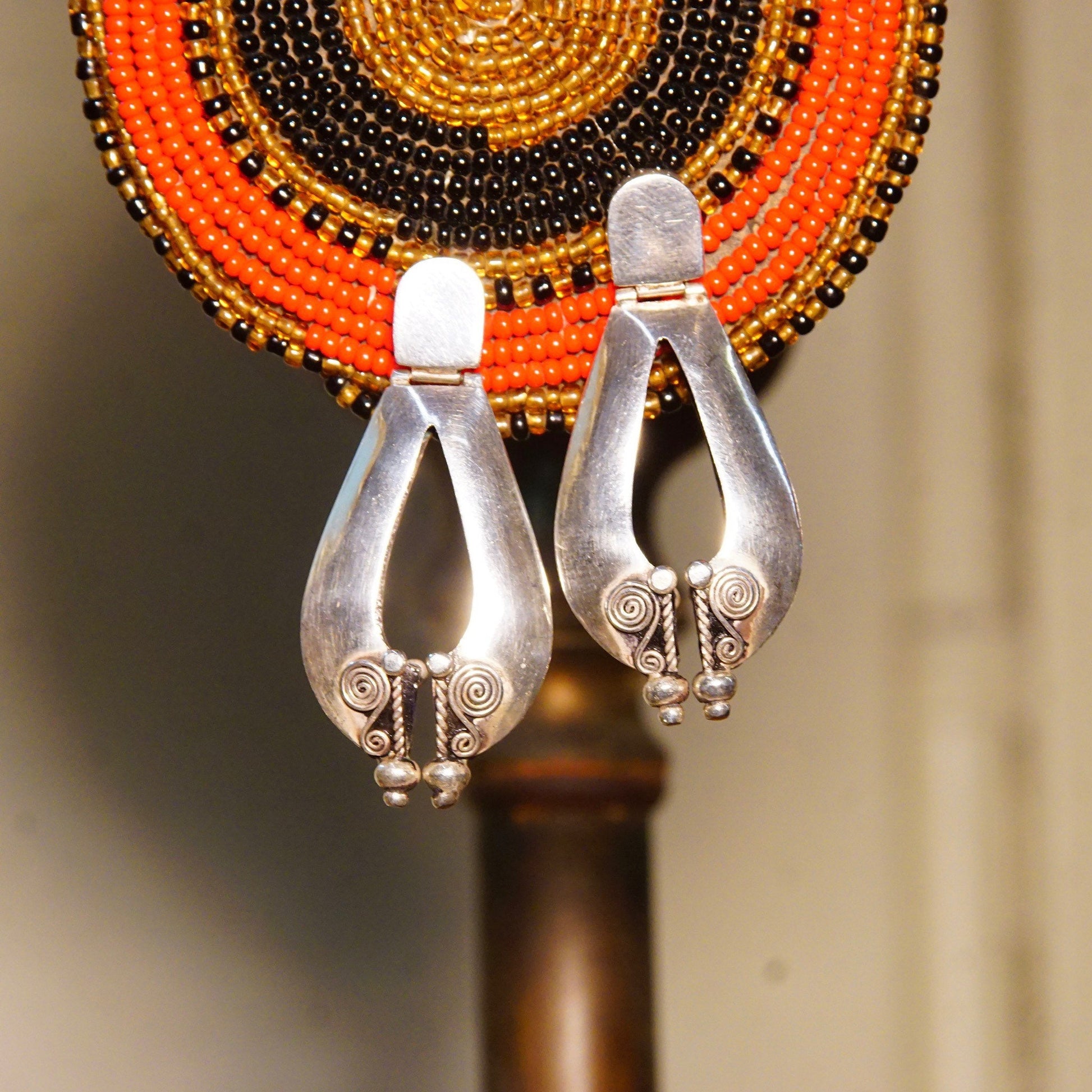 Vintage Bali style sterling silver teardrop dangle earrings with wire wrap designs hanging in front of a colorful beaded wall hanging or hat. The puffed silver earrings are 1 7/8 inches long, making a striking boho fashion accessory crafted from 925 silver.