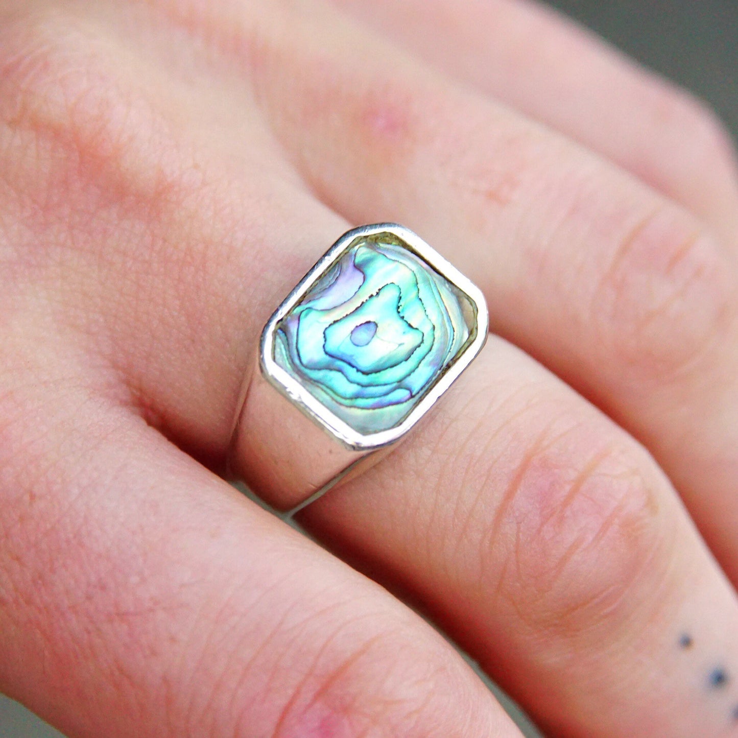 Vintage sterling silver signet ring with iridescent blue-green abalone shell inlay, worn on a finger. Unisex silver abalone jewelry, men's ring size 9 1/2 US.