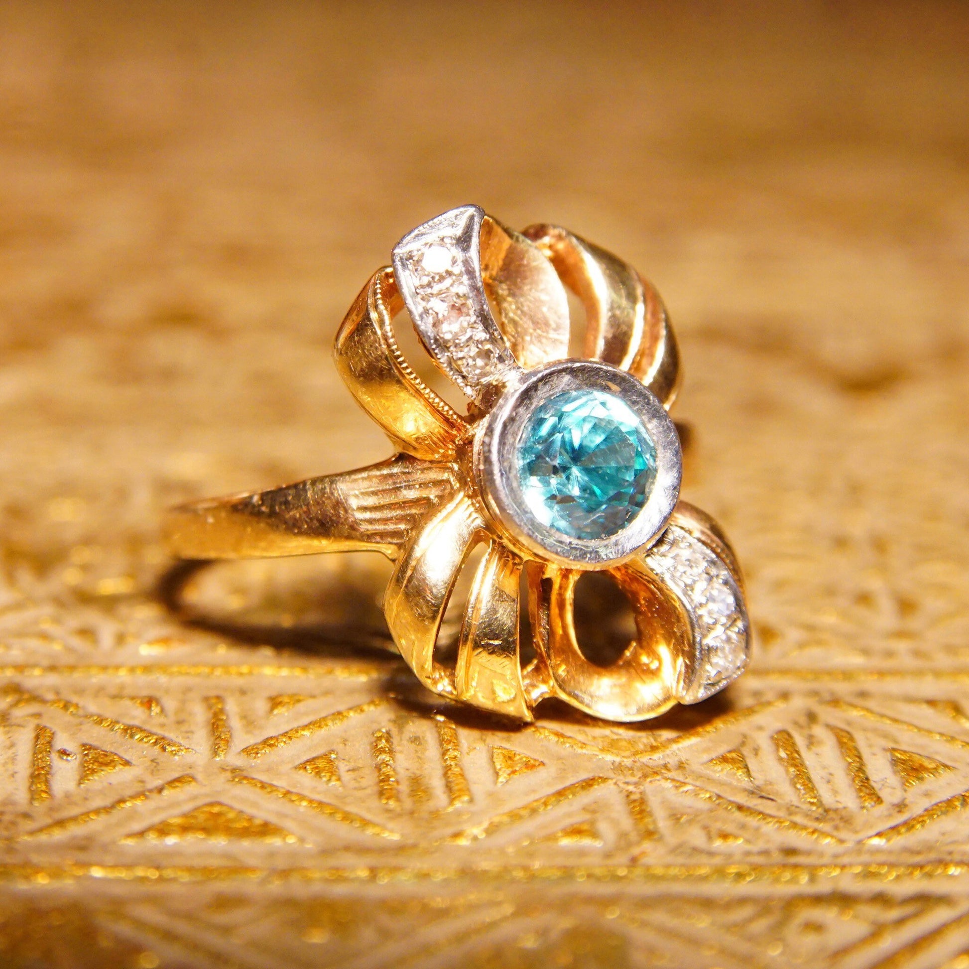 Antique 10K gold ring with blue topaz gemstone and diamond accents in a decorative bow design, crafted by JR Woods & Sons, featuring brilliant blue topaz in the center and white gold ribbon-like setting, size 6 3/4 US.