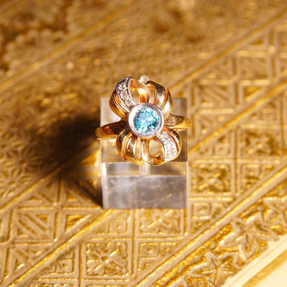 Antique 10K gold blue topaz and diamond bow ring featuring a brilliant blue gemstone in a ribbon setting with white gold accents, made by JR Woods & Sons, size 6 3/4 US.