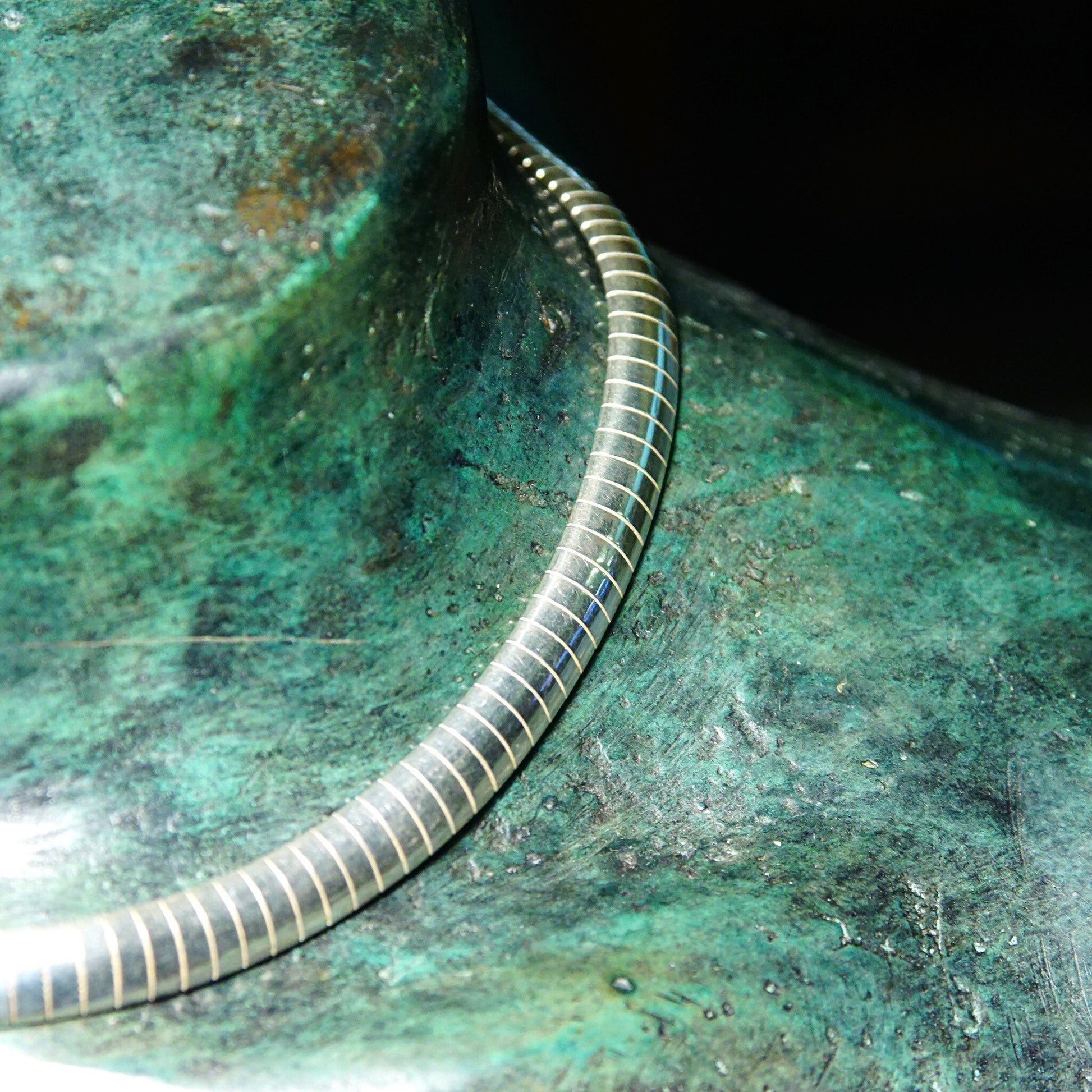 Curved silver omega necklace against an aged green copper background