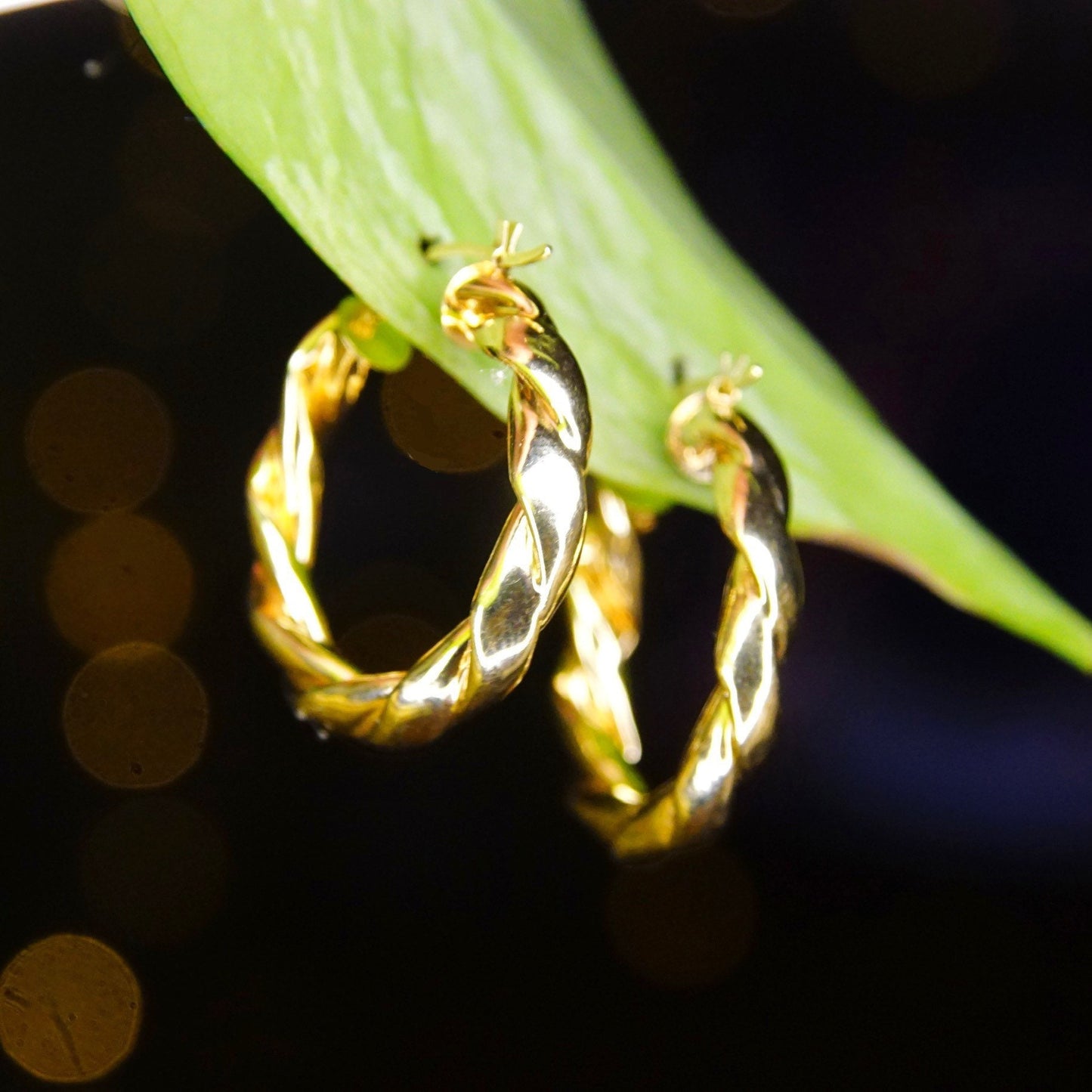 Vintage 14K yellow gold twisted hoop earrings, puffed repousse wreath design, classic 585 gold small to medium sized hoops measuring 17mm in diameter, shown on green leaf.