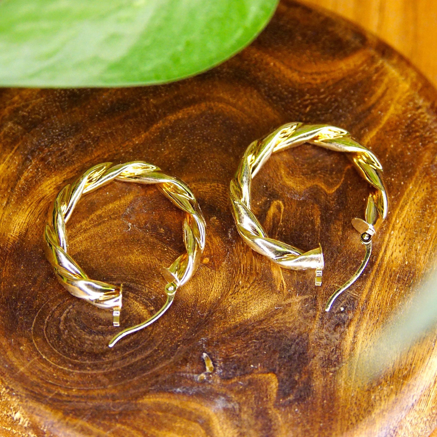 Vintage 14K yellow gold twisted hoop earrings, puffed repousse wreath design, classic 585 gold hoops, small to medium size gold hoops measuring 17mm in diameter, shown on wooden surface with green leaf accent.