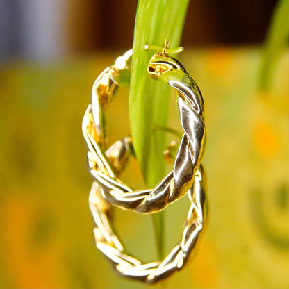 Vintage 14K yellow gold twisted hoop earrings in a small/medium size, featuring a puffed repousse wreath design. The hoops measure approximately 17mm in diameter and have a classic, elegant style. Close-up view focusing on a single earring on a green blurred background.