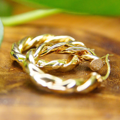 Vintage twisted 14K gold hoop earrings with raised wreath pattern on wooden surface